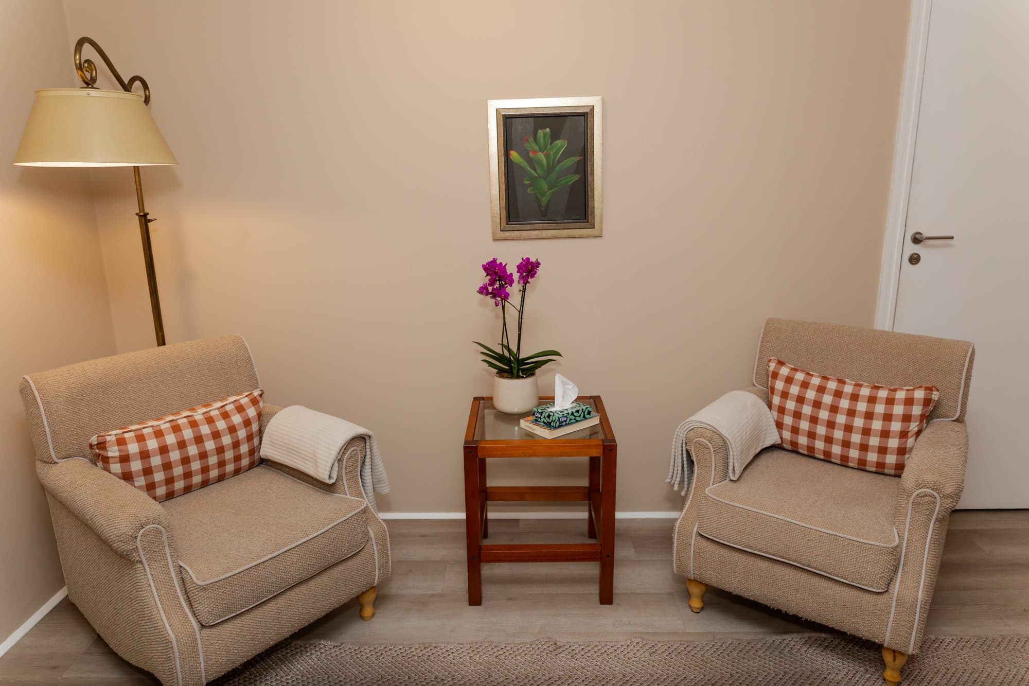 Sala de atendimento com duas poltronas, luminária e orquídea